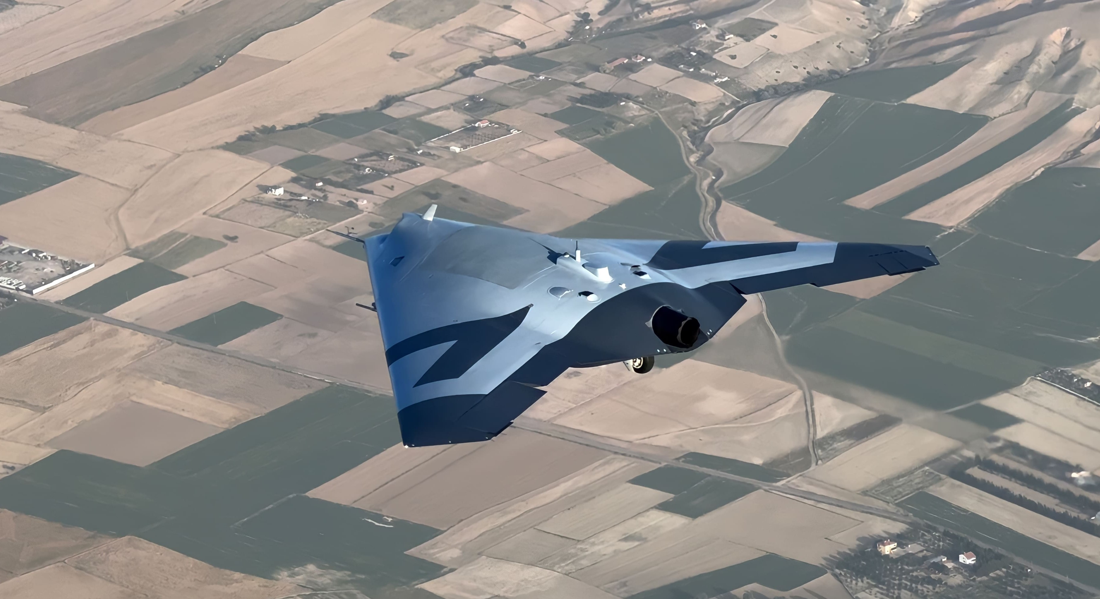 Turkish Aerospace's ANKA III, a jet-powered stealth flying-wing unmanned combat aircraft, in flight over farmland
