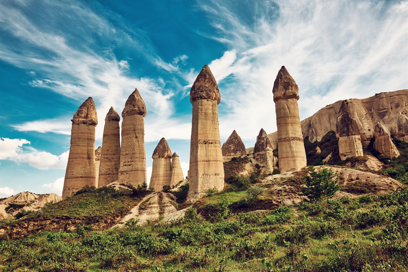 Tall conical fairy chimneys (peri bacaları) of Aşk Vadisi (Love Valley) in Cappadocia, the eroded volcanic tuff rising against a blue Anatolian sky with cirrus cloud