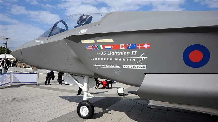 An F-35 Lightning II on static display, with the partner nations' flags painted on the fuselage beside the aircraft's name. The Turkish flag is fifth in the row.