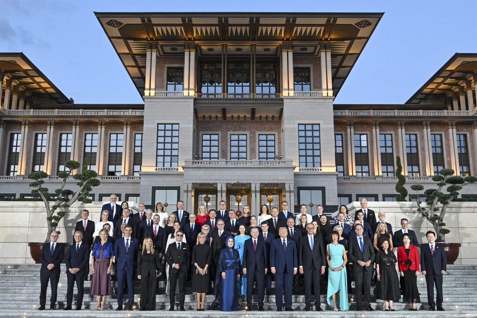 NATO leaders and their spouses gathered for the summit family photograph on the illuminated steps of Türkiye's Presidential Complex at dusk, with President Erdoğan and his wife at the center of the front row.