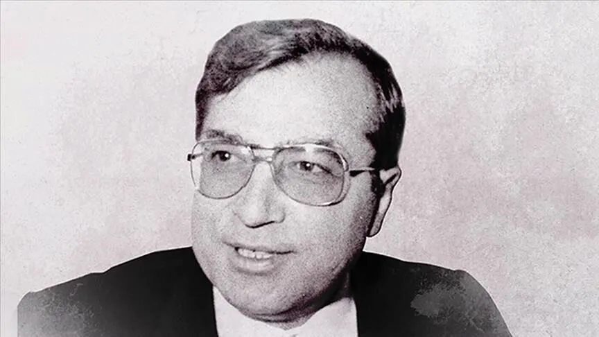 A black-and-white portrait of Dr Sadık Ahmet, wearing metal-framed glasses and a dark suit, looking at the camera with a slight smile.