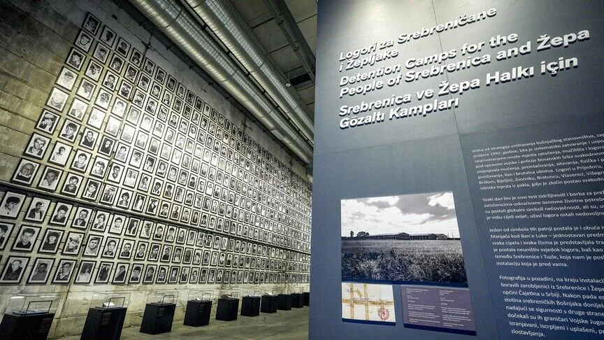 Inside the Srebrenica Genocide Museum, a wall of framed black-and-white portraits of victims beside an exhibit panel captioned in English, Bosnian and Turkish.