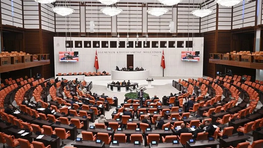 The main chamber of Türkiye's Grand National Assembly in Ankara, its curved rows of orange benches facing the rostrum beneath the wall motto 'Sovereignty belongs unconditionally to the nation.'