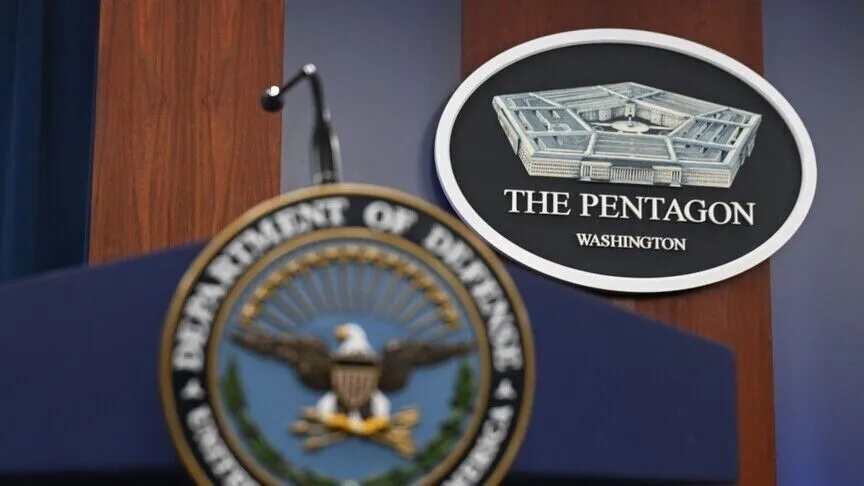 An empty lectern in the Pentagon briefing room, carrying the seal of the US Department of Defense, with a plaque reading The Pentagon, Washington on the wood-paneled wall behind it.