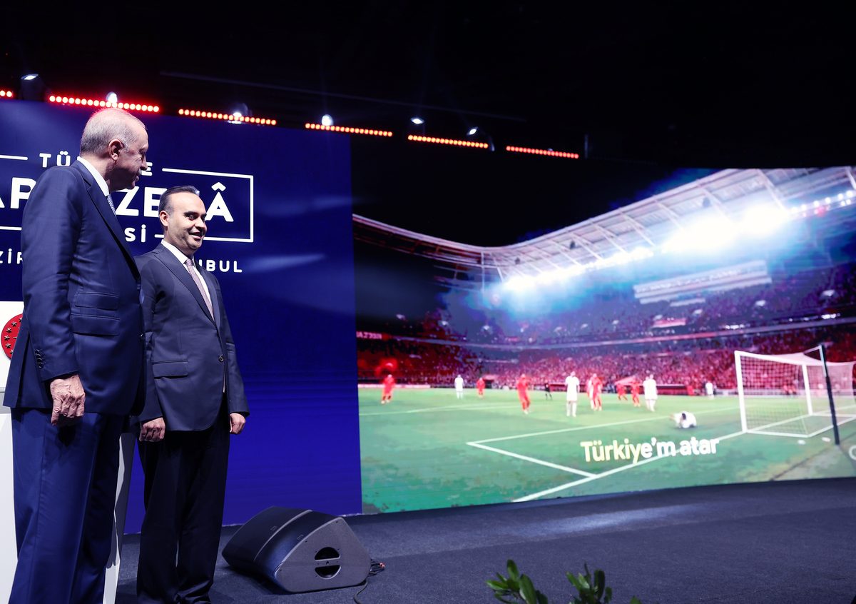 President Recep Tayyip Erdoğan stands on stage at the Türkiye Artificial Intelligence Summit in İstanbul, beside a large video screen.
